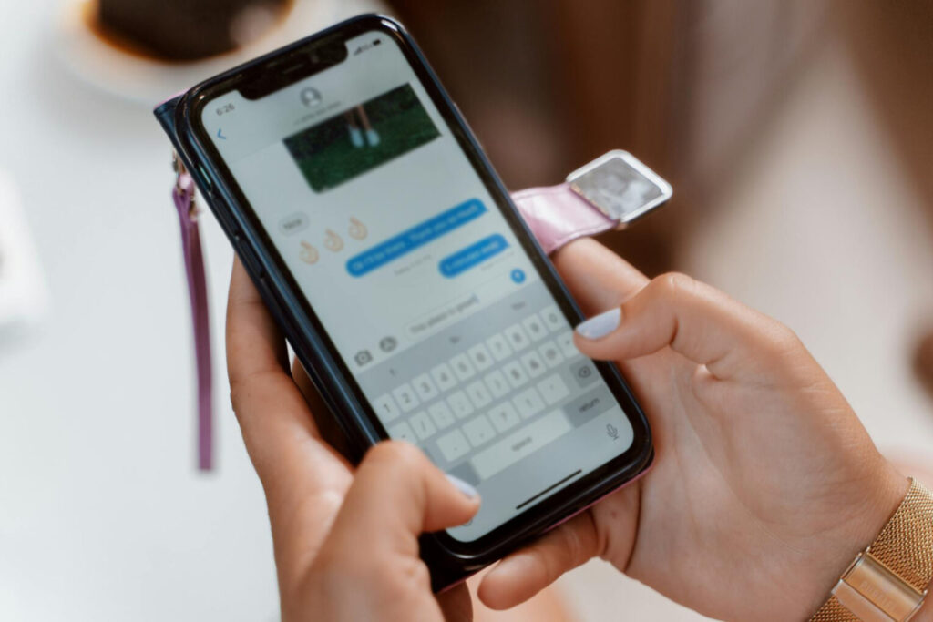 Zbliżenie na dłonie kobiety, która trzyma telefon i pisze wiadomość do kogoś na messengerze
