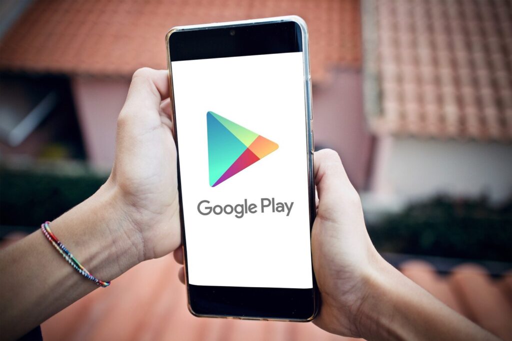 Zbliżenie na dwie ręce trzymające telefon. Na ekranie telefonu widać logo aplikacji sklepu play.