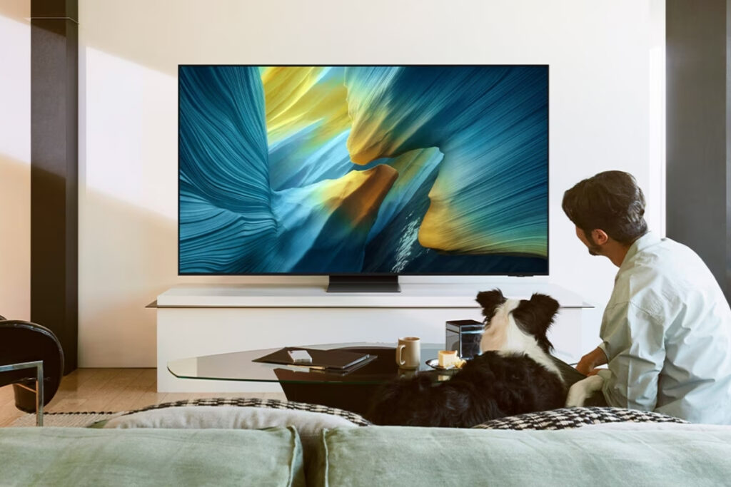 Mężczyzna siedzi przed telewizorem OLED wraz z psem na kanapie.