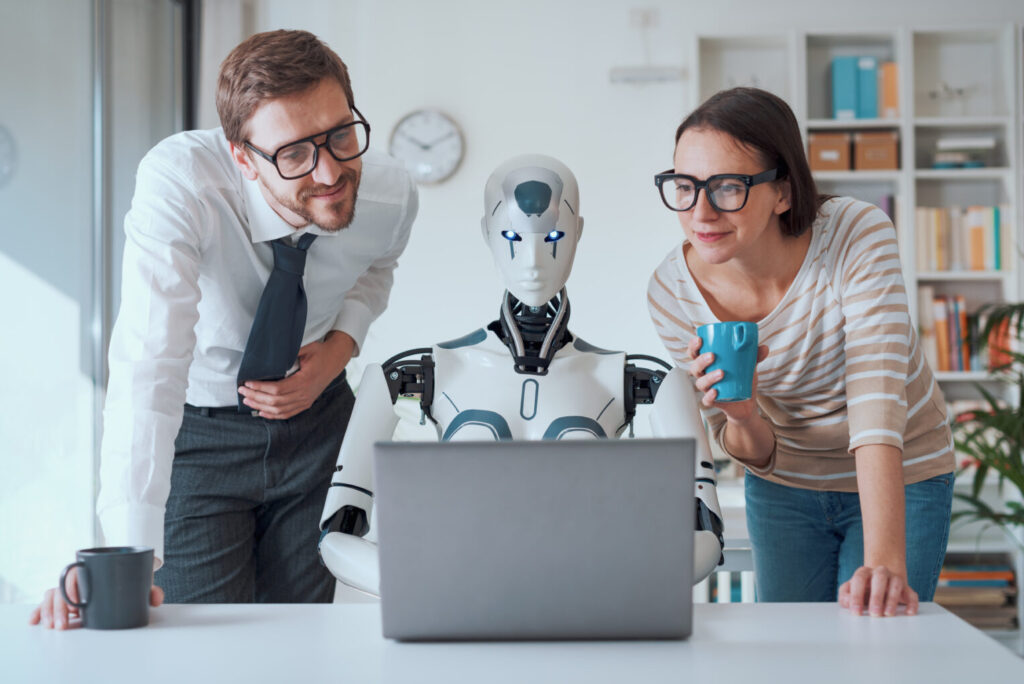Dwie osoby patrz na ekran laptopa. po srodku siedzi robot ai i cos robi