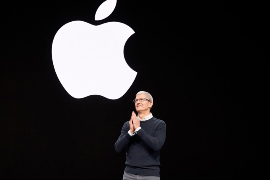 Na scenie stoi człowiek i mówi przez mikrofon, a z tyłu wielkie logo apple
